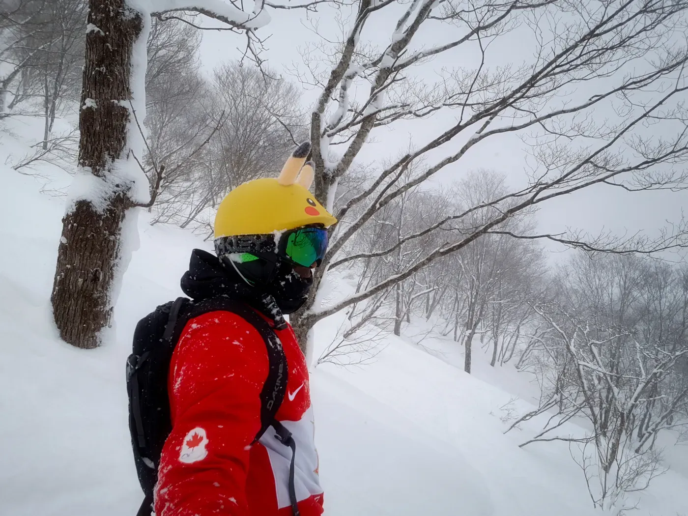 Hombre con chaqueta roja y casco de Pikachu entre árboles cubiertos de nieve en el valle de Hakuba, Japón.